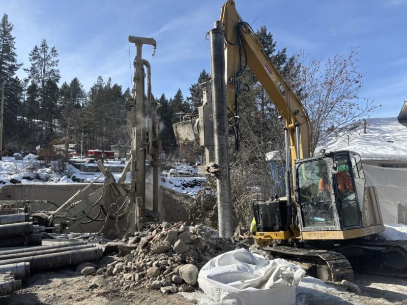 Track-mounted drill rig installing micropiles with CAT excavator support on a winter Pacific Northwest construction site